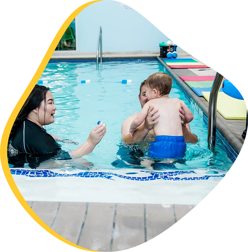 Parent helping a young child build water comfort during a swim lesson at FINS Swim School.