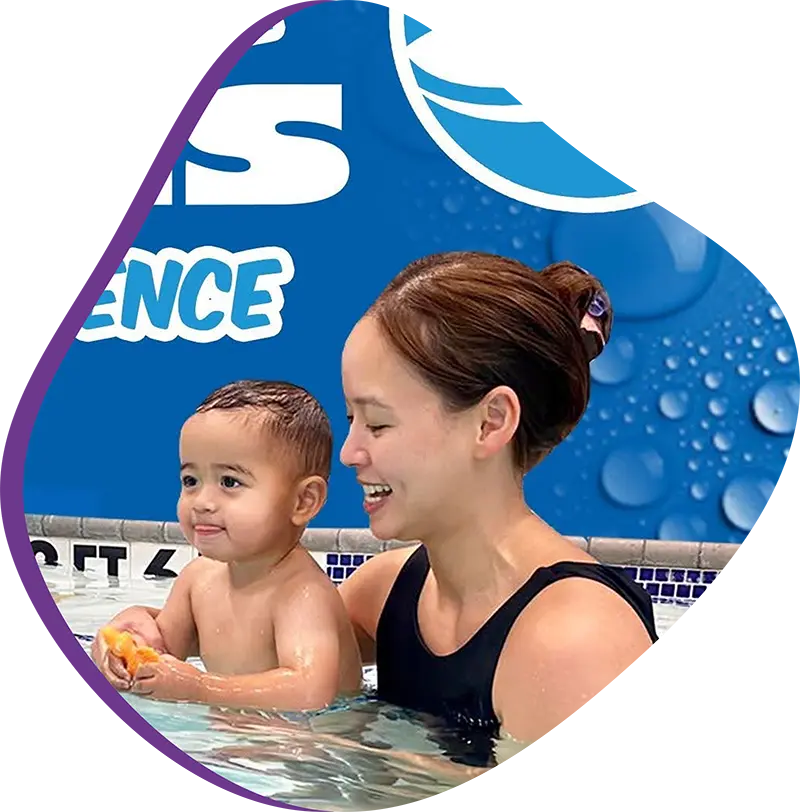 Parent assisting baby during infant swim lesson at FINS Swim School—The Woodlands indoor pool.